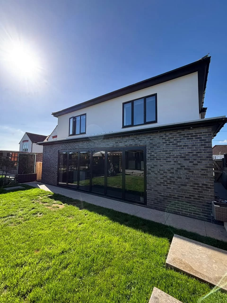 Completed dark brick rear extension with black framed glazing and rendered upper floor